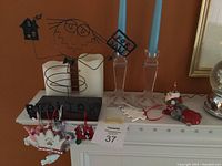Photo of decorative candles, wooden boxes, and Christmas ornaments placed on a white shelf against an orange wall.