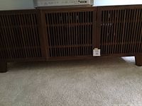 Front view of the wooden cabinet showing wide slatted front doors and low profile design set on short block legs
