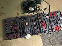 Full view of the open folding carry case with all tools arranged in molded compartments along with black yard spotlight coiled beside it.