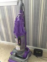Full view of Dyson DC07 Animal upright vacuum cleaner and Zenith digital clock radio on carpeted floor against striped wall.