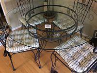 Overall view of the round glass top kitchen table with four iron frame chairs featuring printed cushions and gold sun face accents.
