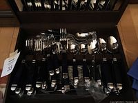 Photo of flatware pieces including forks, knives, and spoons with blue handles on black tray