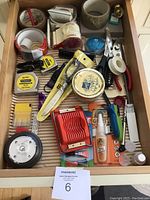 Overview of drawer with multiple household tools and accessories including measuring tapes, scissors, tapes, egg slicers, flashlight, stapler, glue and more.