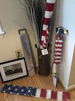Shows the umbrella stand holding several American flags on poles and decorative branches plus George Washington at Valley Forge print leaning by the wall. The What-a-Light panel is visible on the floor along the wall.