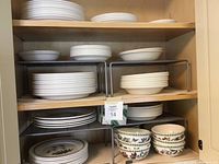 Cabinet shelves with stacks of plain white plates and bowls alongside patterned bowls.