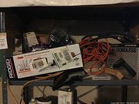 Overview photo of lot on shelf showing Rigid reciprocating saw box, extension cord, drill box, and other items.