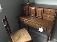 Front-right angled view of wooden secretary desk and wooden chair with rush seat.