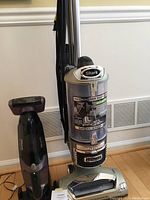 Shark upright vacuum and cordless handheld vacuum together showing size and color contrast