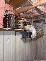 Woven baskets displayed on wooden shelves hung from the ceiling with metal chains, showing variety of sizes and styles including some large basket handles.