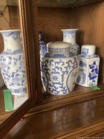 Photo showing front view of multiple blue and white porcelain ginger jars and vases inside wooden cabinet