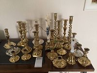 Front view showing a variety of brass candle holders with traditional and twisted designs, a silver-plated candelabra, and a ceramic-handled brass bell.