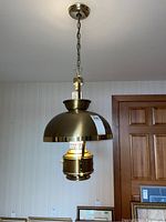 Full view of the brass hanging light fixture showing the dome-shaped brass cover, the glass globe, and the hanging chain attached to the ceiling mount.