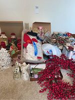 Wide view showing assortment of pillar candles, Christmas-themed candles, white porcelain Christmas tree, decorative ribbons, and artificial red berry wreath.