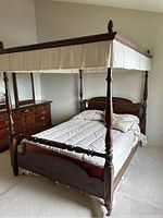 Front left view of dark wood canopy bed with beige bedding on carpeted floor