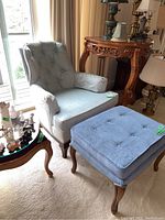 Wide angle of antique style armchair and matching footstool on carpet near table and window.