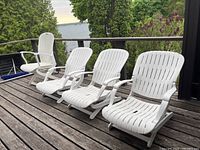 Four white Allibert reclining yard deck chairs on a wooden deck with view of trees and water.