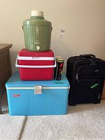 Photo showing all the items in the lot, stacked coolers and the suitcase to the right.