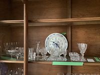 Shelf displaying assorted cut crystal glassware and the blue and white porcelain Bulova clock in the background.
