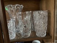 Photo showing the five crystal vases placed closely on a shelf within a wooden cabinet.