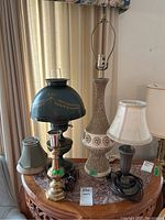Photo showing four lamps of varying sizes and styles, two with shades and two without, sitting on a marble-topped table.
