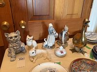 Image showing all items in the lot: three cat figurines (two Beswick, one blue and white), two Lladro figurines (woman and child with ducks), brass goose figurine and small covered porcelain dish.