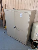 Front view of the beige painted metal cabinet with two doors and chrome locking handle.