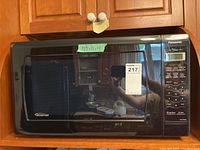 Closed front view of Panasonic microwave with control panel and sticker indicating dimensions 23.5x18x14 inches.
