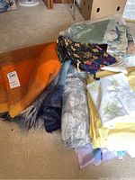 View showing two mohair blankets - one orange with checkered pattern and one blue, plus various other textile items including pillowcases, fabric bags, and seat cushions.