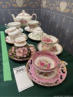 Photo showing seven teacups with saucers and Sadler teapot with floral designs arranged on a table.