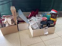 Boxes containing travel mugs, plastic cups, strainers, and other kitchen items.