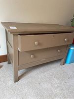 Front angle view of a solid painted wooden dresser with two drawers and round knobs, showing wear and drawer slightly open.