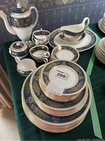Group view of all pieces on green tablecloth showing teapot, sugar bowl, creamer, cups, saucers, plates, gravy boat, and tray