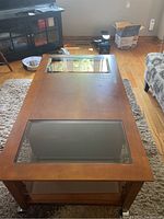 Top down view of rectangular wood coffee table with two inset glass panels on top, resting on a beige shag rug.