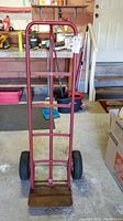 Front view of the red metal movers dolly standing upright in a garage, showing tubular metal frame and platform.