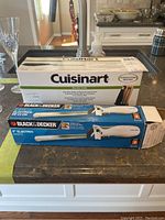 Photo showing Cuisinart electric knife box and two Black & Decker electric cutters boxes on kitchen counter.