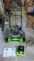 Overview of snow thrower frame, auger housing, handle sections, battery, charger and manuals on garage floor