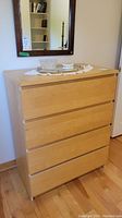Front view of light wood Ikea 4 drawer dresser with decorative items on top.