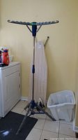 Laundry drying rack next to washing machine with ironing board and laundry basket in background