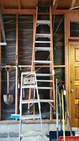 View of 8-foot wooden extending ladder and 5-foot aluminum step ladder standing against garage wall with other tools stored around.