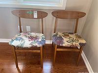 Two Mid-Century Modern wood chairs with oval backrests and floral patterned upholstered seats on wooden legs.