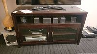 Full front view showing wood media stand with glass doors and five small speakers on top shelf.