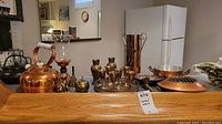 Various copper, brass and silverplate metalware items including kettle, candleholder, hammered vases and pitcher, brass serving goblets and a silver tray.