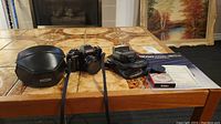 Overview of all items on a table including camera in the middle, camera case, flash unit, Kenko filter, manual, and lens cap.