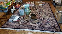Full view of large patterned area rug on wood parquet floor, surrounded by household items.