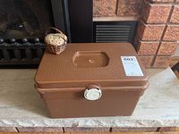 Closed view of brown plastic sewing box with floral fabric pin cushion in woven basket on top