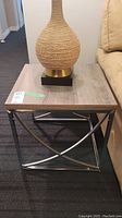 Side table with light wood grain laminate top and silver metal frame with geometric crossed design on the sides.