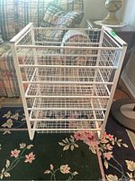 Front view of white metal storage cabinet with five removable wire grid baskets in a living room setting.