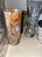 Onyx vase with brown, orange, and white layers, smooth cylindrical shape, standing next to clear glass vase with bubble texture and other items.