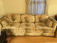 Front view of the 3 seater sofa showing floral upholstery with three seat and back cushions and two bolster pillows.