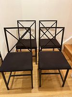 Four metal dining chairs with black cushioned seats arranged inside a room near a staircase.